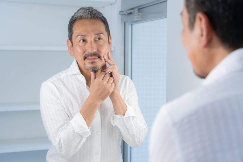 洗顔後の清潔な肌に、セラミドやナイアシンアミド配合の化粧水を丁寧になじませる男性。乾燥による老化の進行を遅らせるため、「洗顔後3分以内の即保湿」を徹底し、肌のハリを守るための「未来への投資」としての習慣を実践しているシーン。