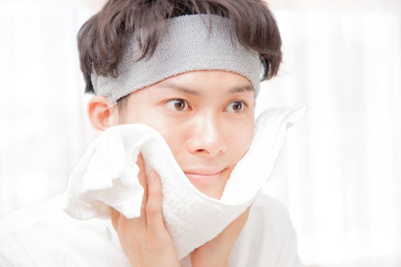 髭剃り後、タオルを肌に押し当てるようにして優しく水分を拭き取る男性。「ゴシゴシ拭かない」ことで、傷つきやすい状態の肌への二次ダメージを防ぐ様子。