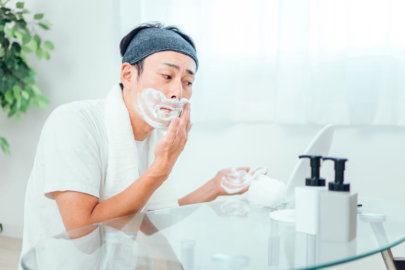 シェービング前にたっぷりの泡やジェルを顔に広げ、ヒゲを柔らかくして刃の滑りを良くしようとする男性。肌表面の負担を最小限に抑えるための重要な準備ステップ。